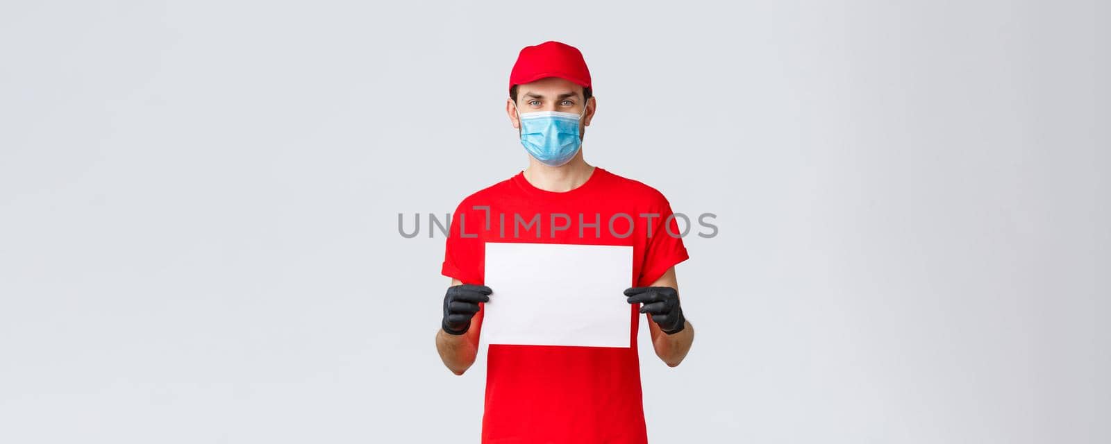 Covid-19, self-quarantine, online shopping and shipping concept. Express delivery guy during coronavirus tell stay safe home, buy internet, holding blank piece paper for your info, wear face mask by Benzoix