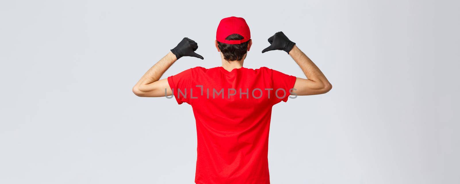 Covid-19, self-quarantine, online shopping and shipping concept. Back view of courier pointing at his t-shirt to show carrier company logo, courier promote service of delivery during coronavirus by Benzoix