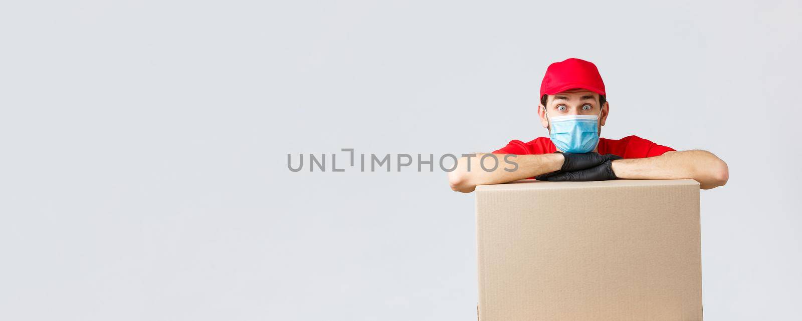 Packages and parcels delivery, covid-19 quarantine and transfer orders. Worried and confused courier in red uniform, gloves and face mask, lean on order box and look surprised camera.