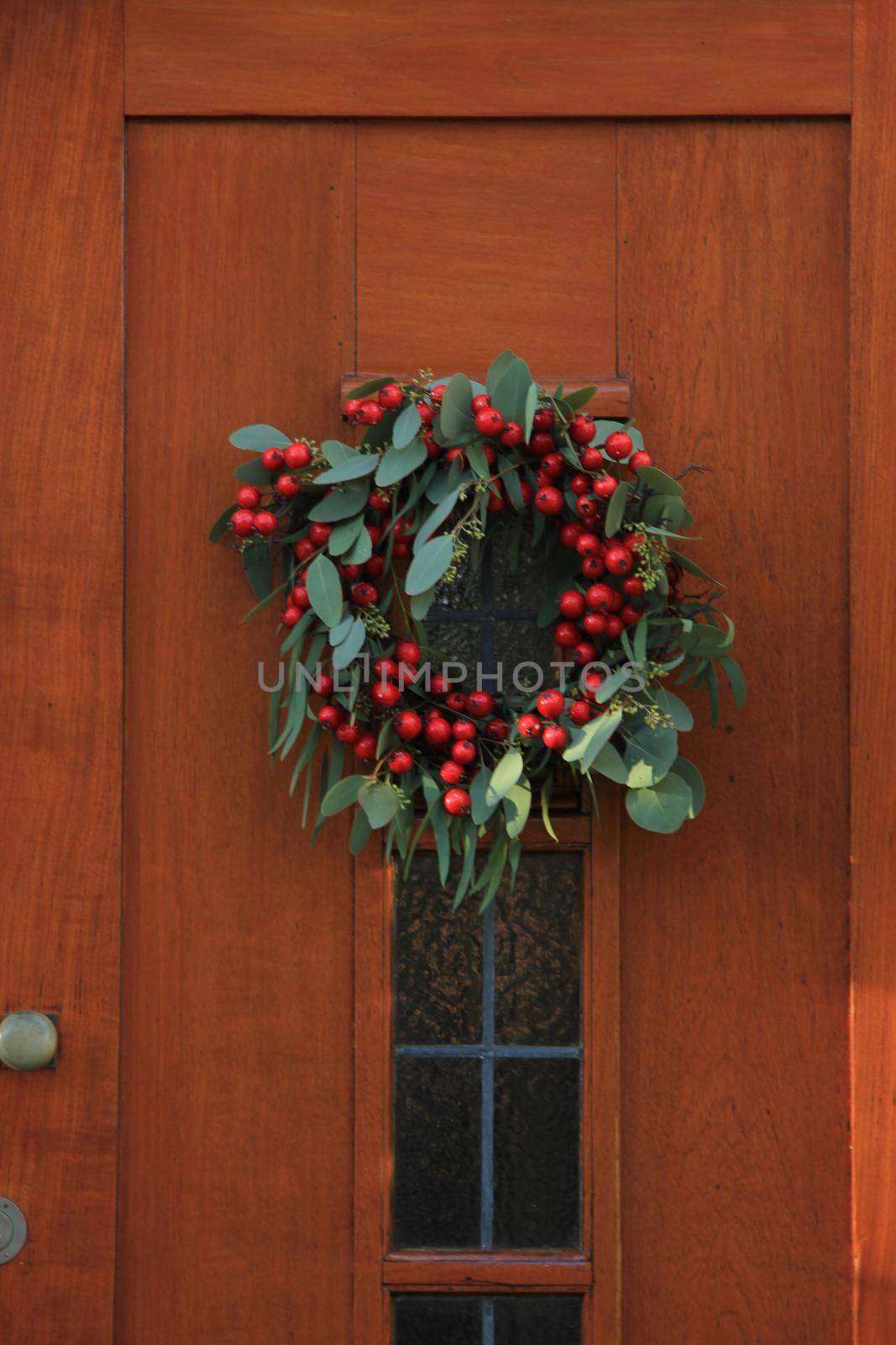 Berry christmas wreath with decorations on a door by studioportosabbia