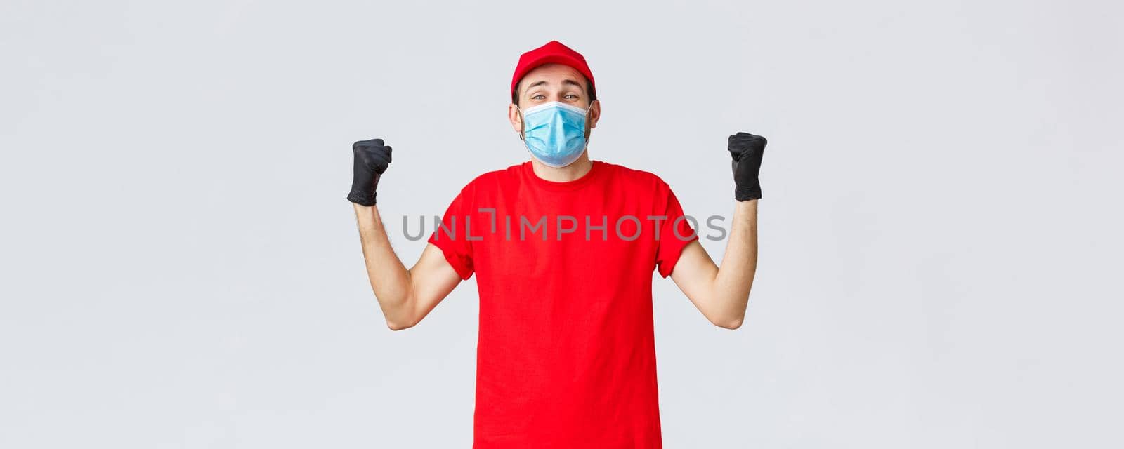 Covid-19, self-quarantine, online shopping and shipping concept. Excited delivery man feel rejoice and happiness, fist pump in celebration, success, achieve goal, wear medical mask and uniform cap.