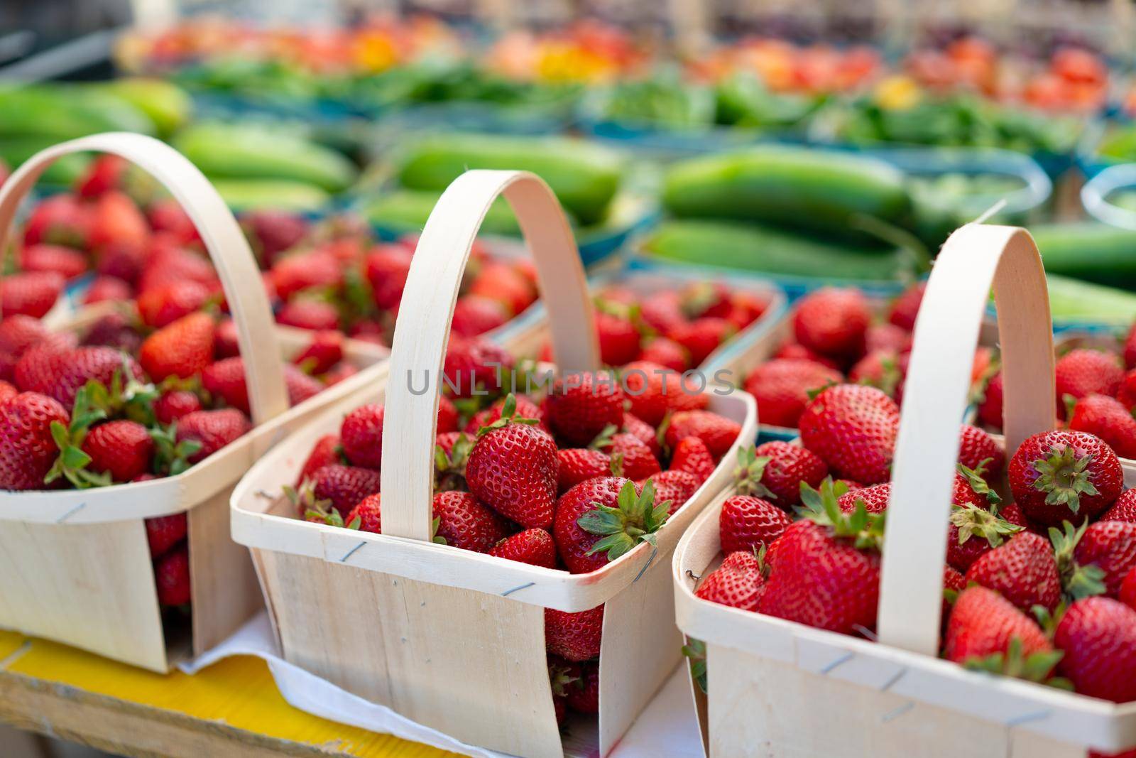 Strawberries for sale on vegetables market. Raw juicy strawberry in wooden basket standing on market display with other fruit and berry on background. Seasonal sweet berry