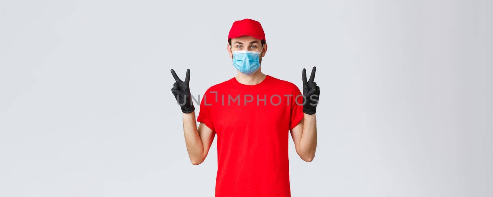 Covid-19, self-quarantine, online shopping and shipping concept. Cute delivery guy in red uniform, face mask and gloves, stay positive in coronvirus outbreak, show peace sign, courier deliver goods by Benzoix