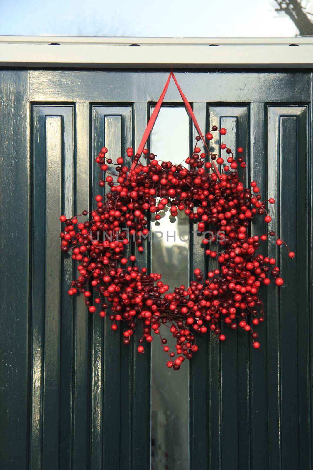 Berry christmas wreath with decorations on a door by studioportosabbia