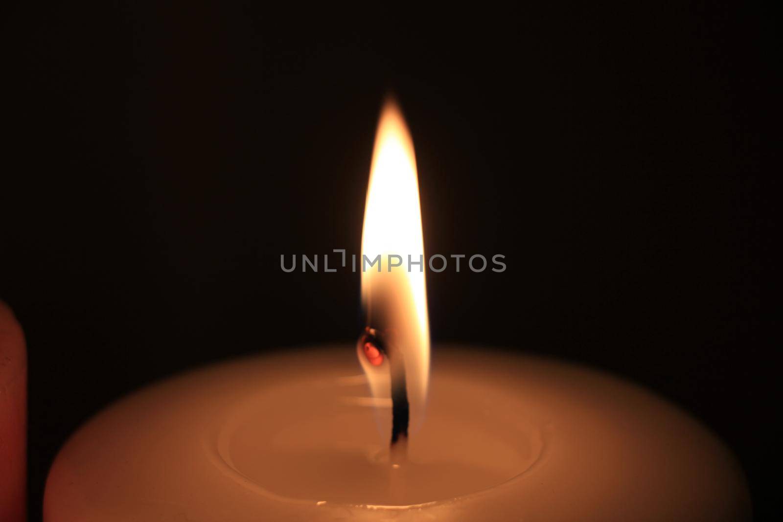 Burning candle in closeup, big flame and melted wax