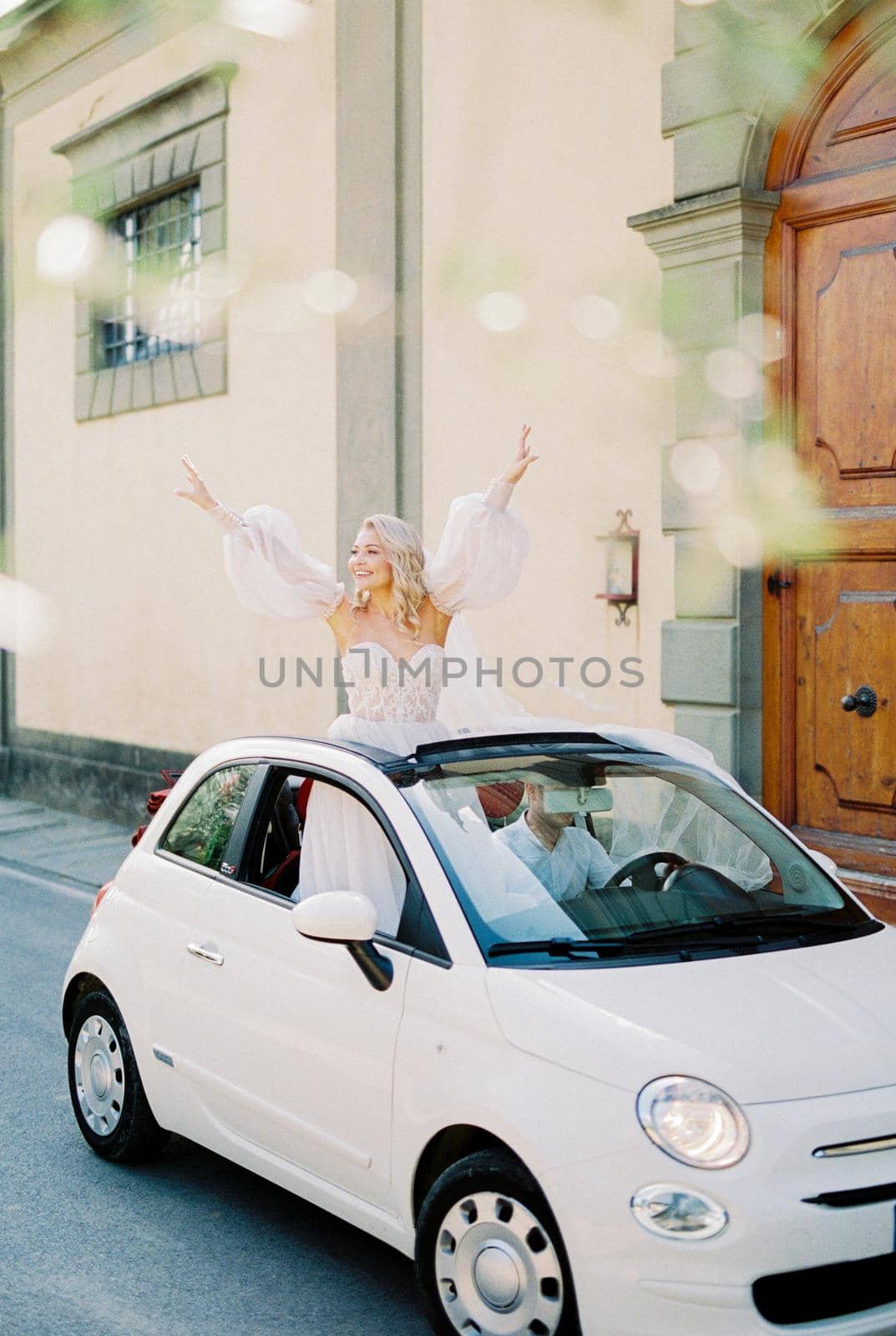 Bride leaned out in the hatch of the Fiat 500 car with her hands up. High quality photo