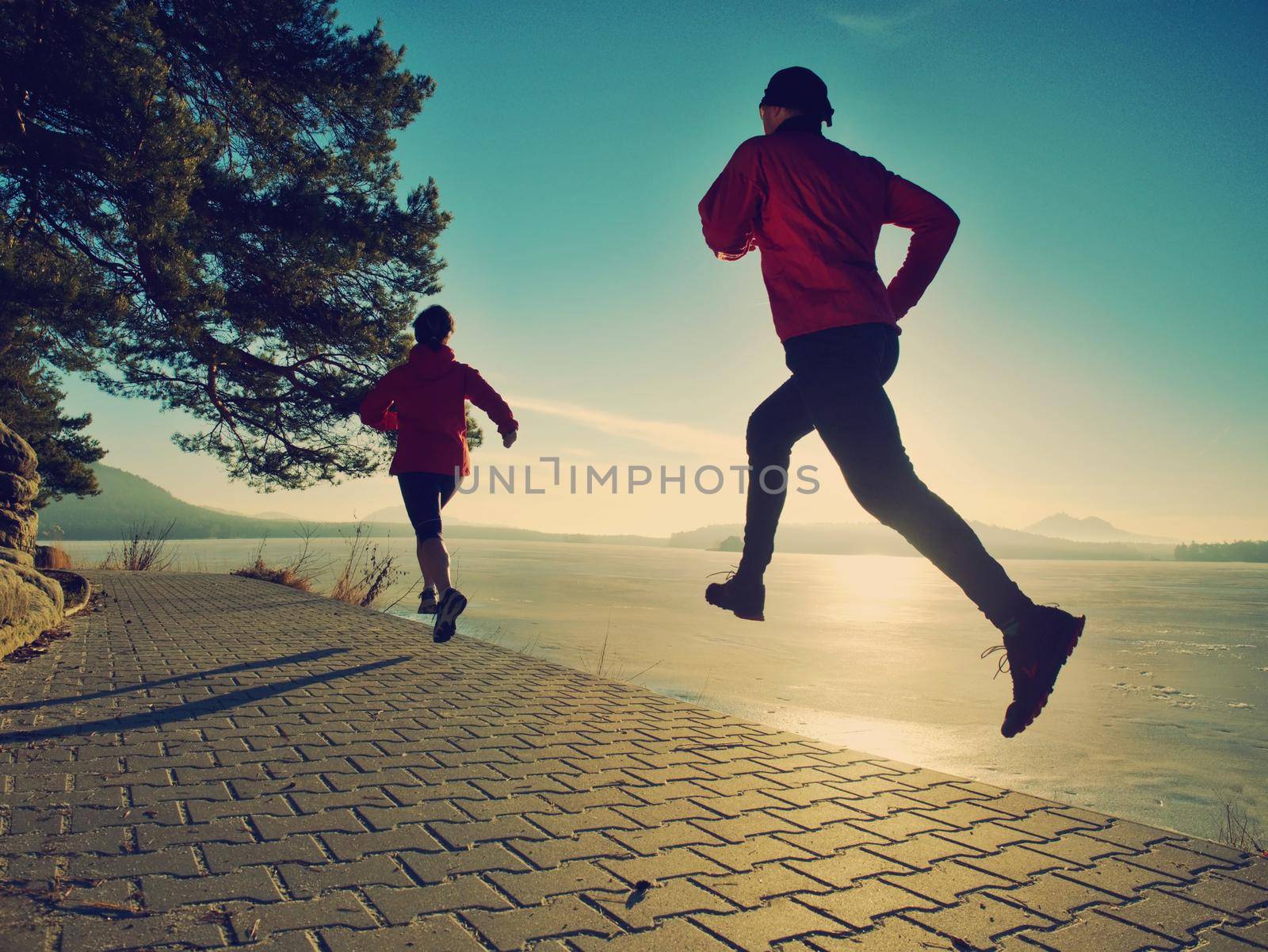 Young couple of runners during regular outdoor morning workout run at frozen lake..