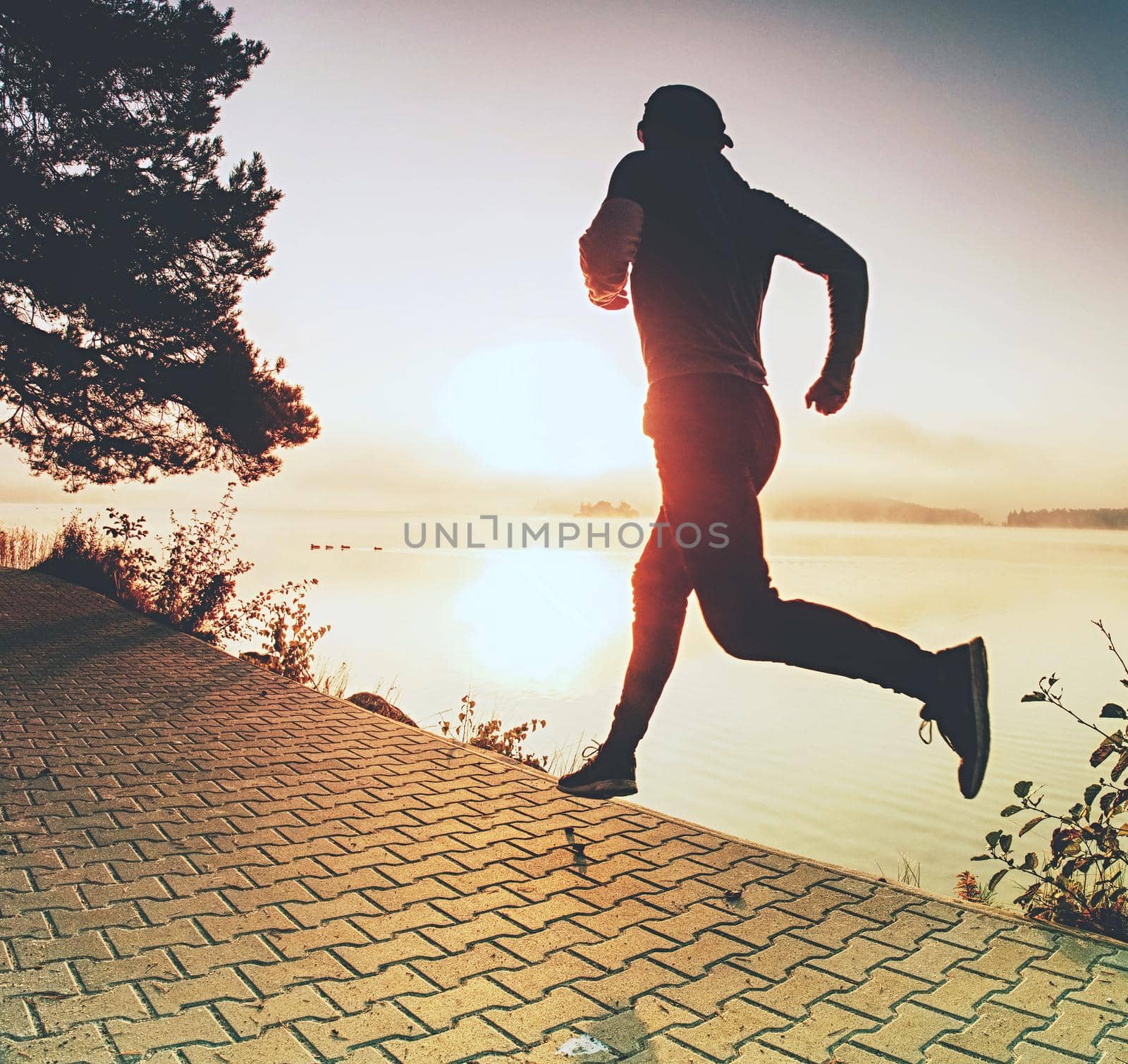 Tall slim man is running along lake in park in sunny daybreak. by rdonar2
