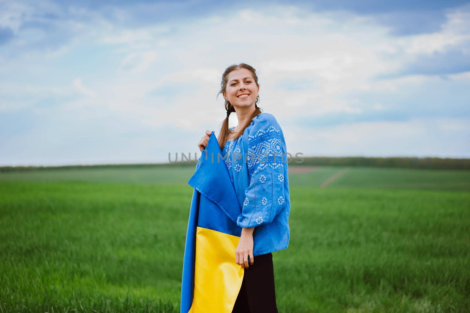 Beautiful ukrainian woman with national flag on green field background. Young lady in blue embroidery vyshyvanka. Ukraine, independence, freedom, patriot symbol, victory in war. High quality photo