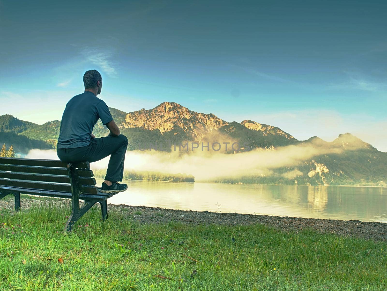 Alone man sits on bench beside an azure mountain lake. Man relax  by rdonar2