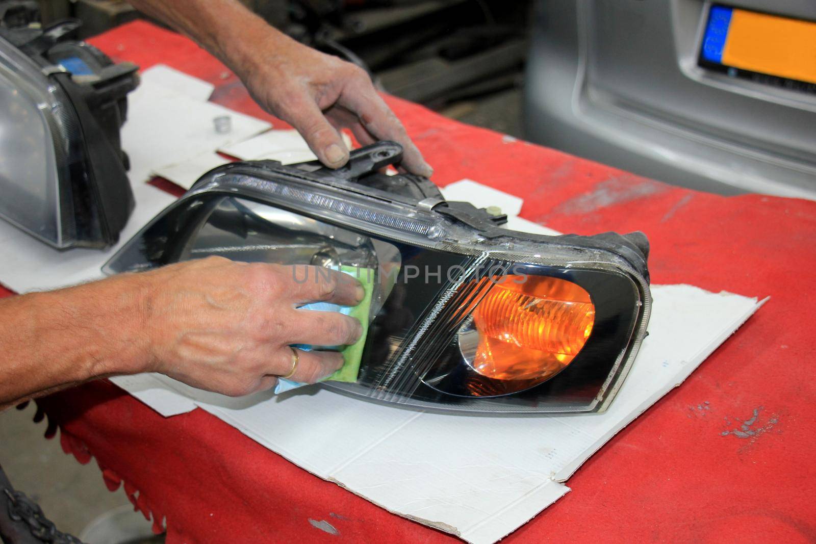Man refurbishing a car headlight with clear coating by studioportosabbia