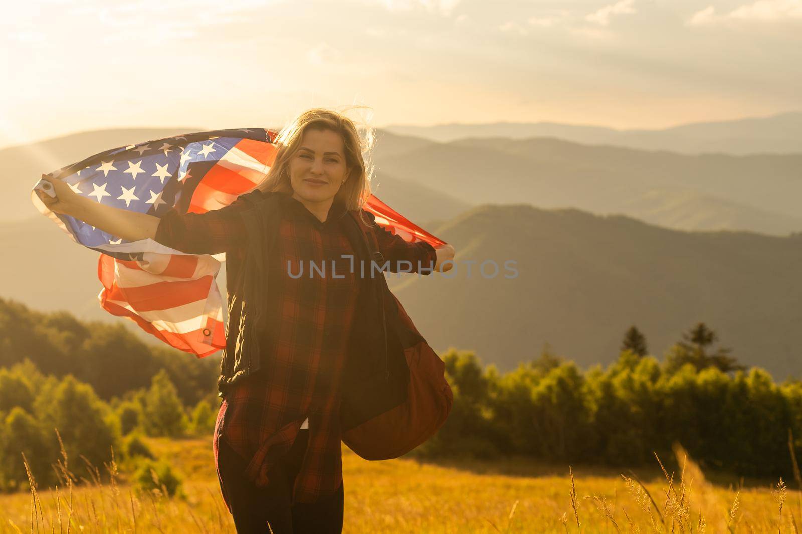 Young woman holding American flag on sky background.