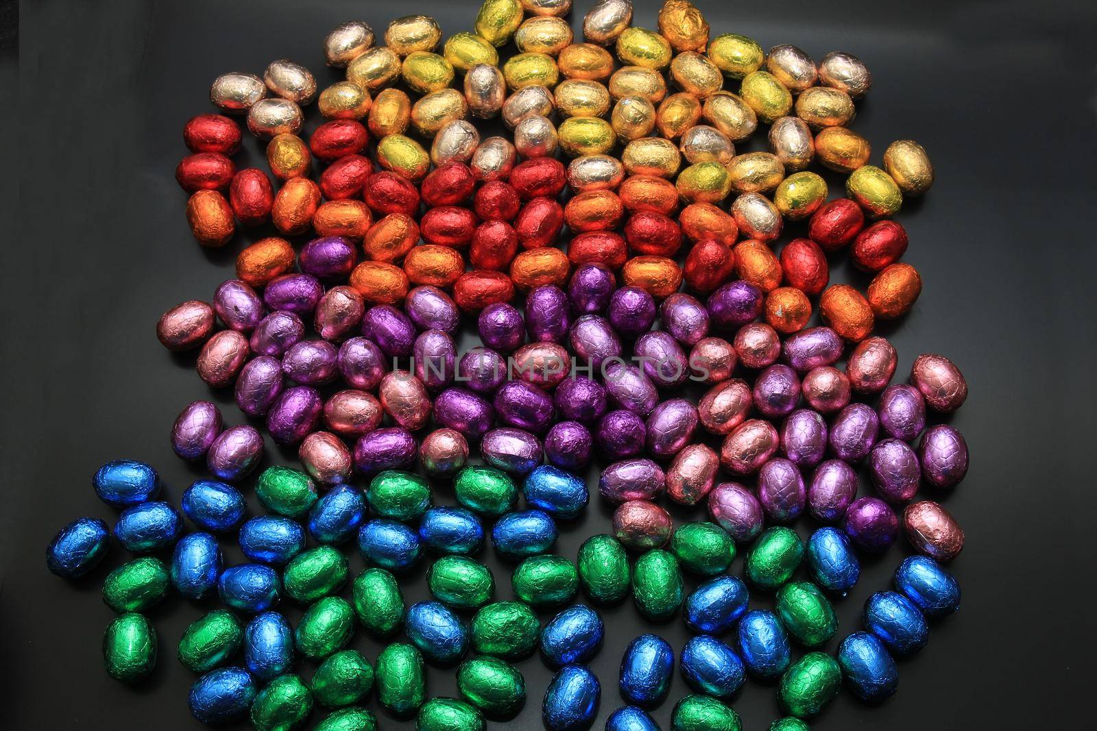 group of foil wrapped chocolate easter eggs in rainbow colors by studioportosabbia