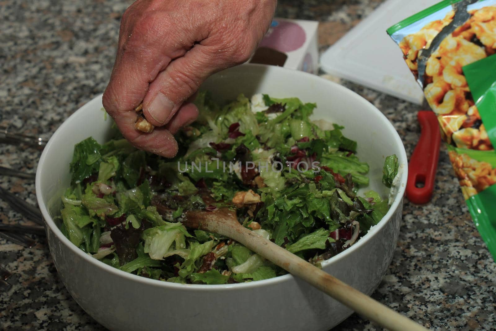 Man preparing a green salad with walnuts, goat cheese and oil by studioportosabbia