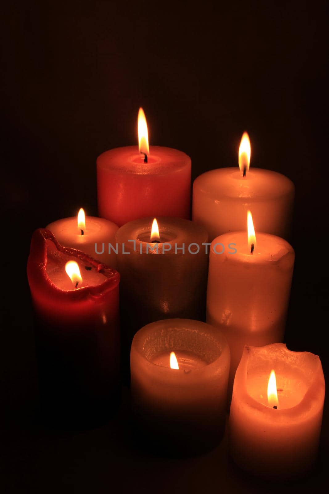 Group of burning candles in different heights and colors by studioportosabbia