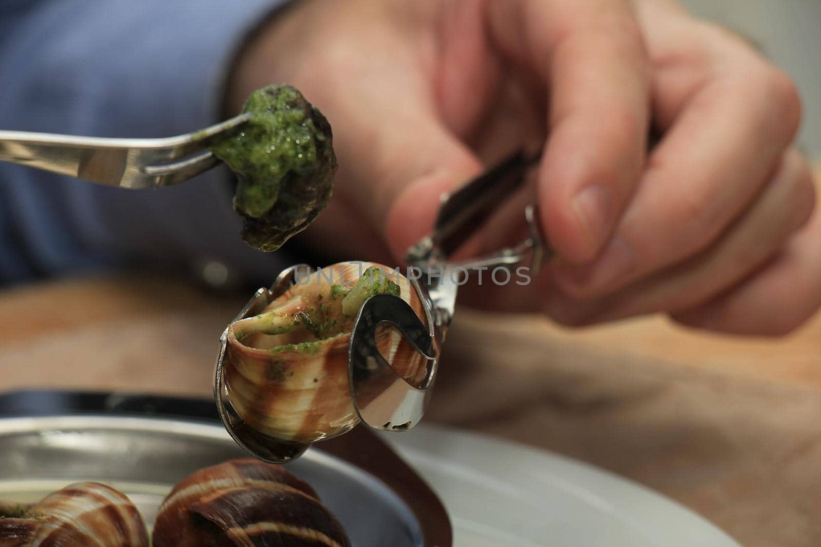 Man eating escargots de Bourgogne using a special tong and a snail fork