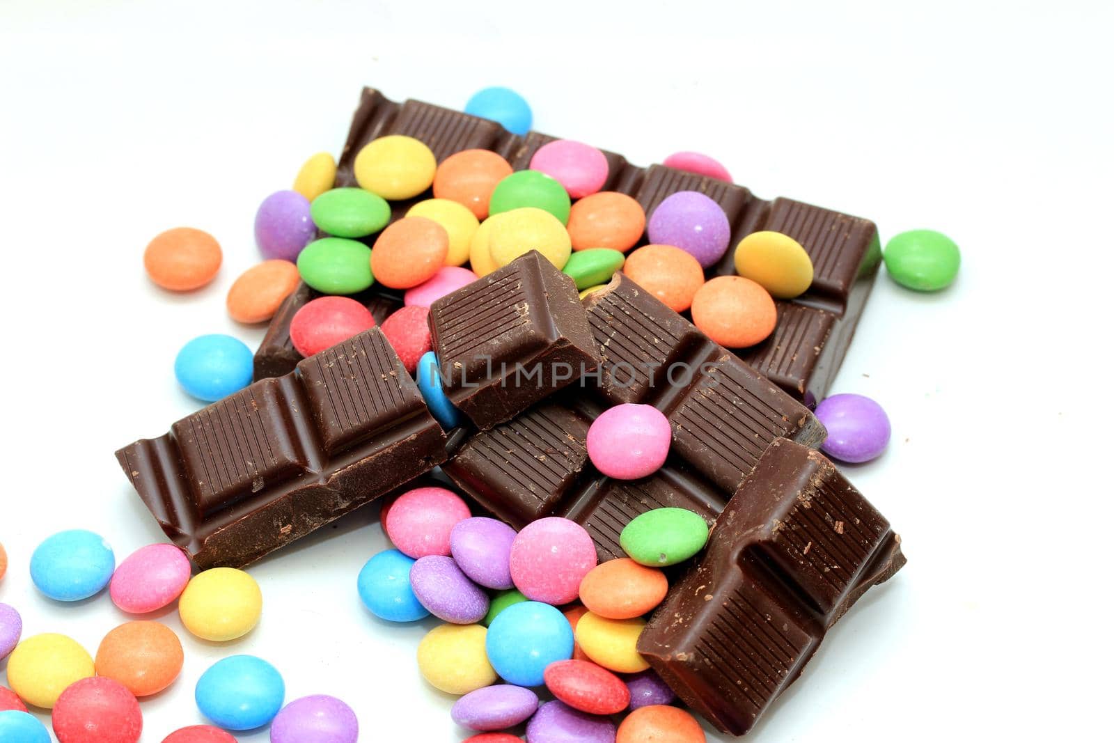 Chocolate filled candies in various bright colors and pieces of a chocolate bar by studioportosabbia