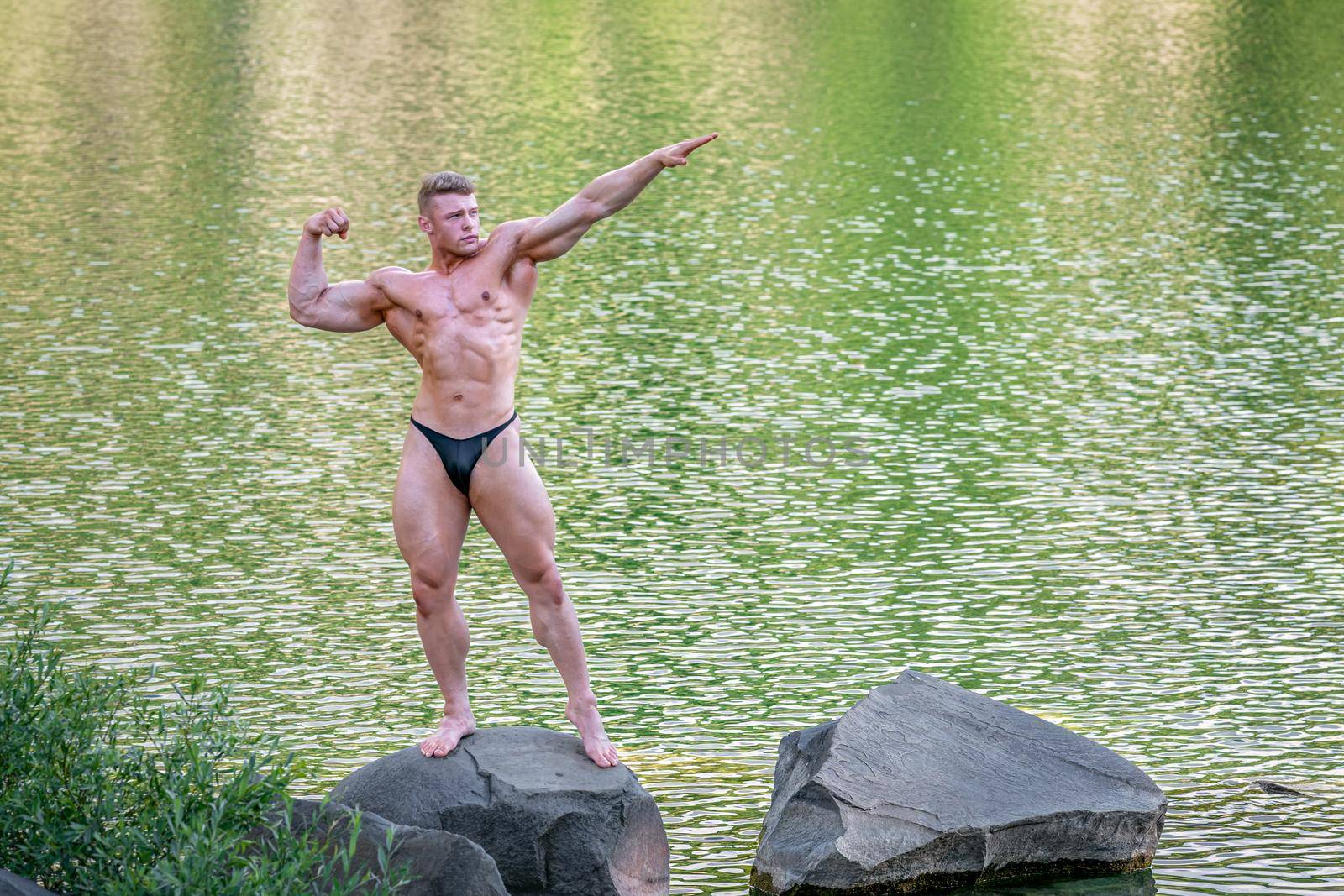 male bodybuilder by the water in nature.