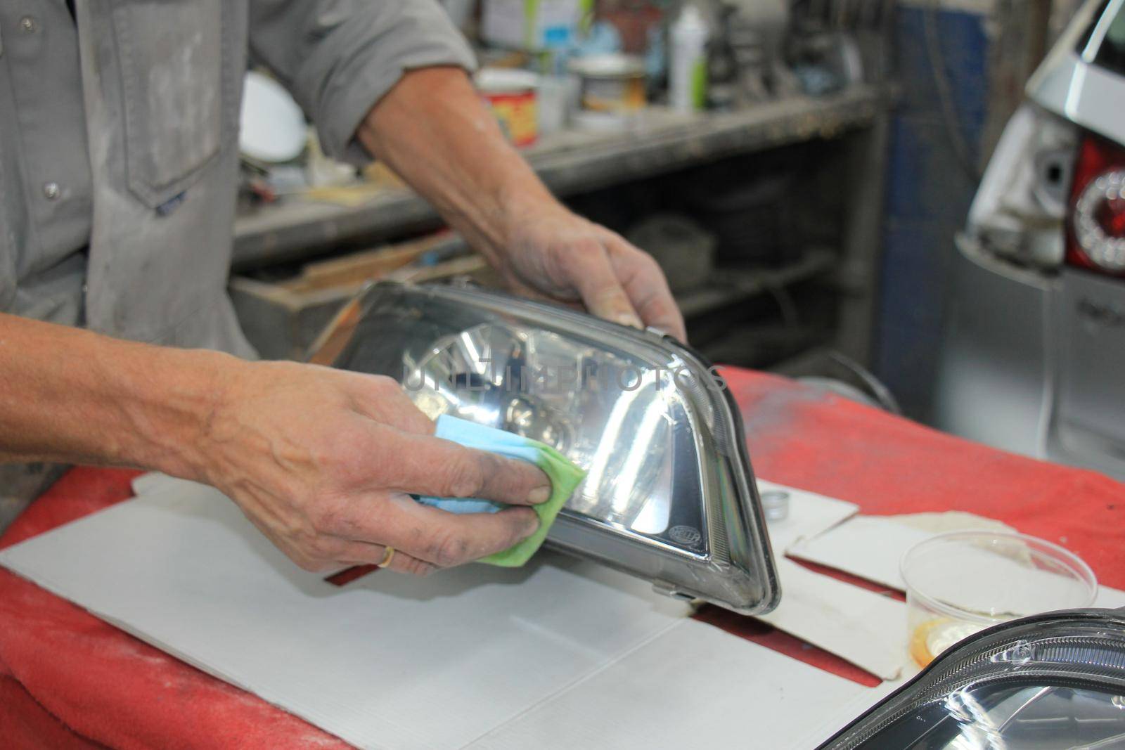 Man refurbishing a car headlight with clear coating by studioportosabbia