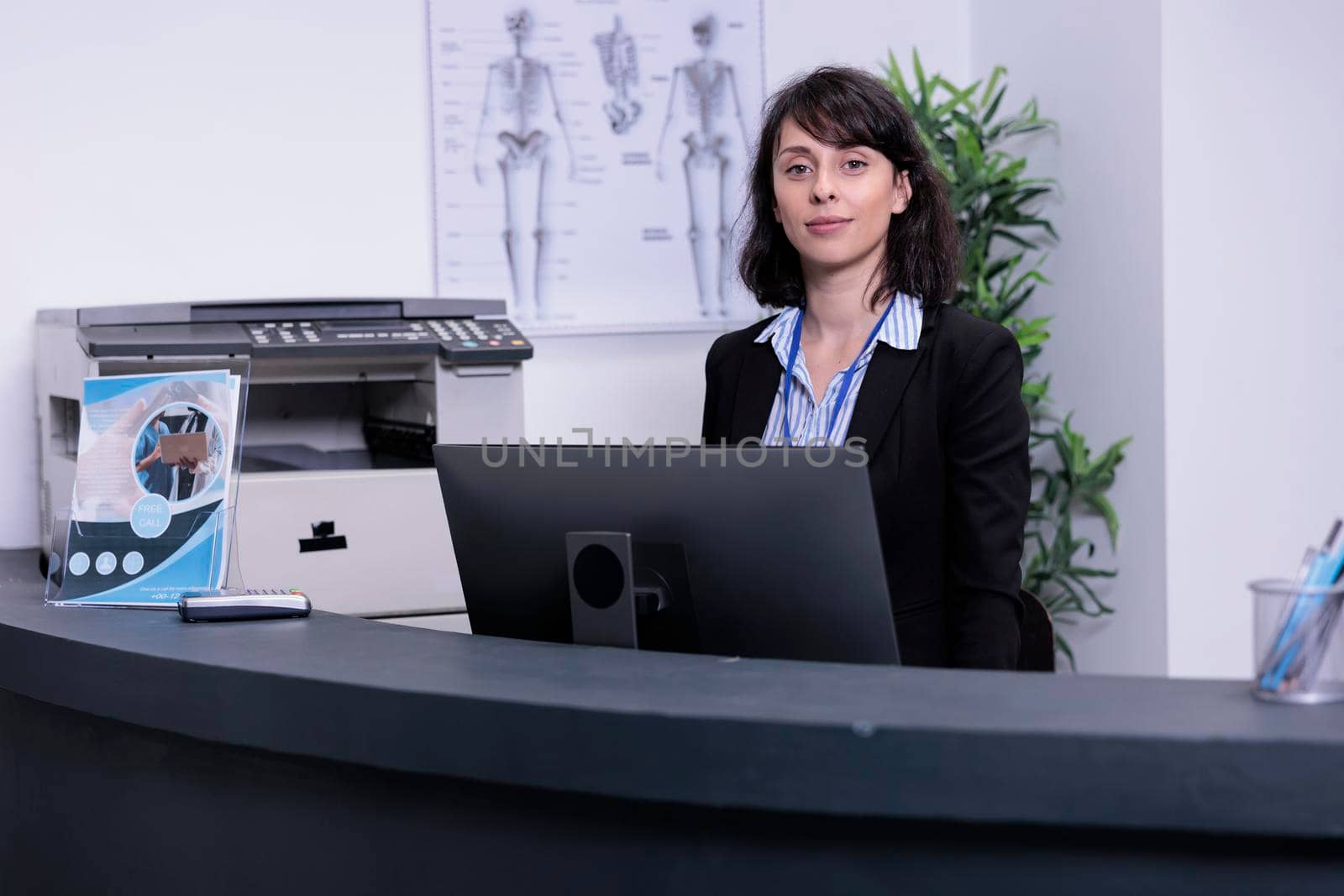 Portrait of smiling hospital receptionist standing at front desk waiting for appointments in private hospital. Professional healthcare worker greeting patients in private practice clinic lobby.