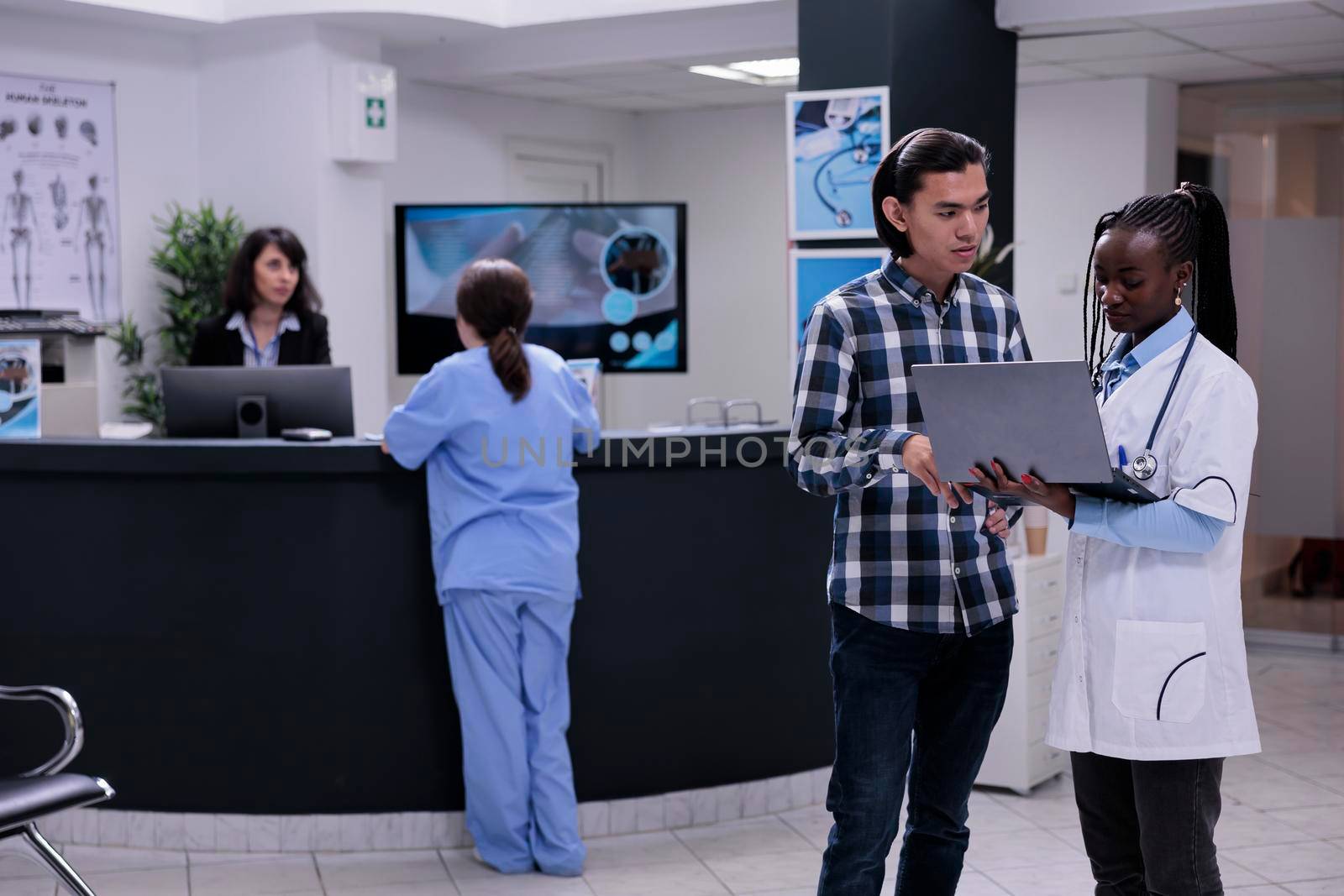 African american medical doctor holding laptop presentig lab results to asian patient by DCStudio