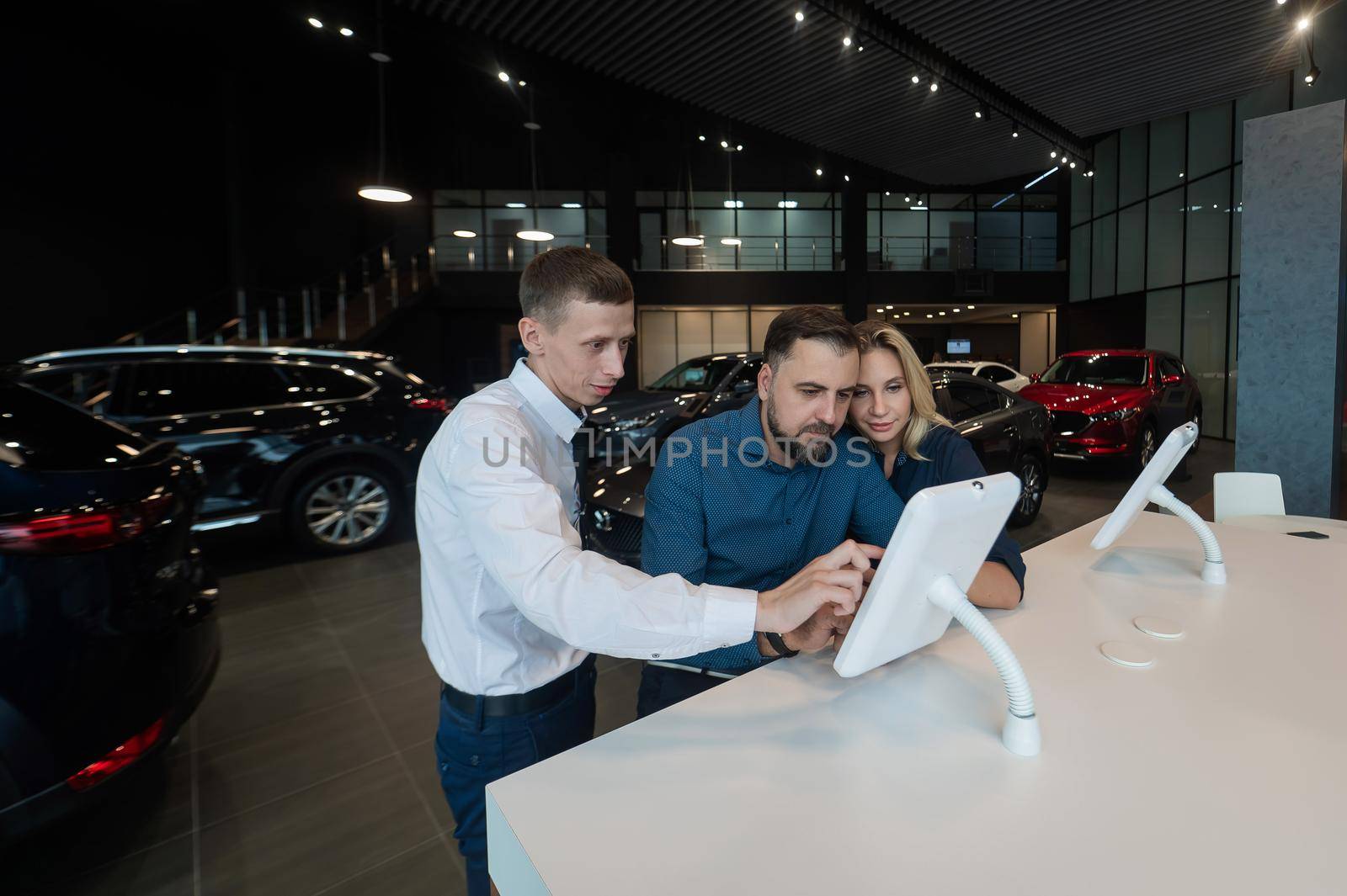 Caucasian married couple chooses a car in a car dealership on digital tablets