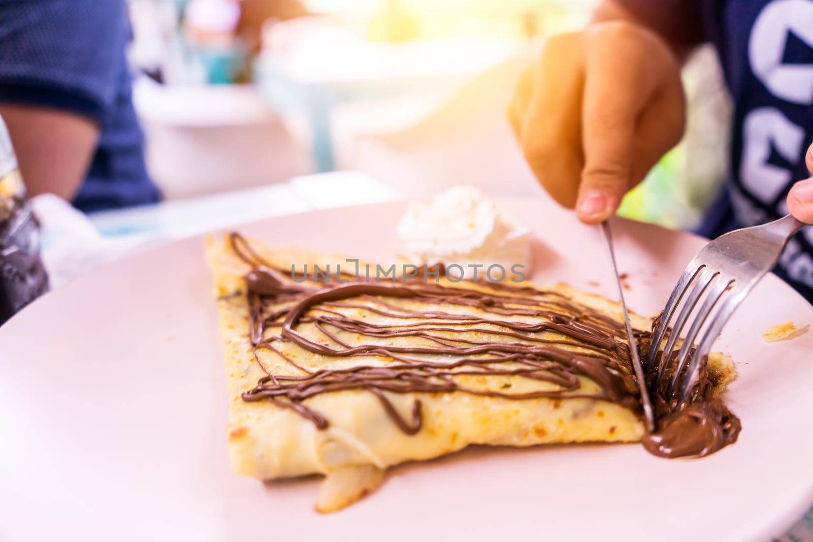 Closeup to the hands of a boy eating crepes with chocolate by cfalvarez