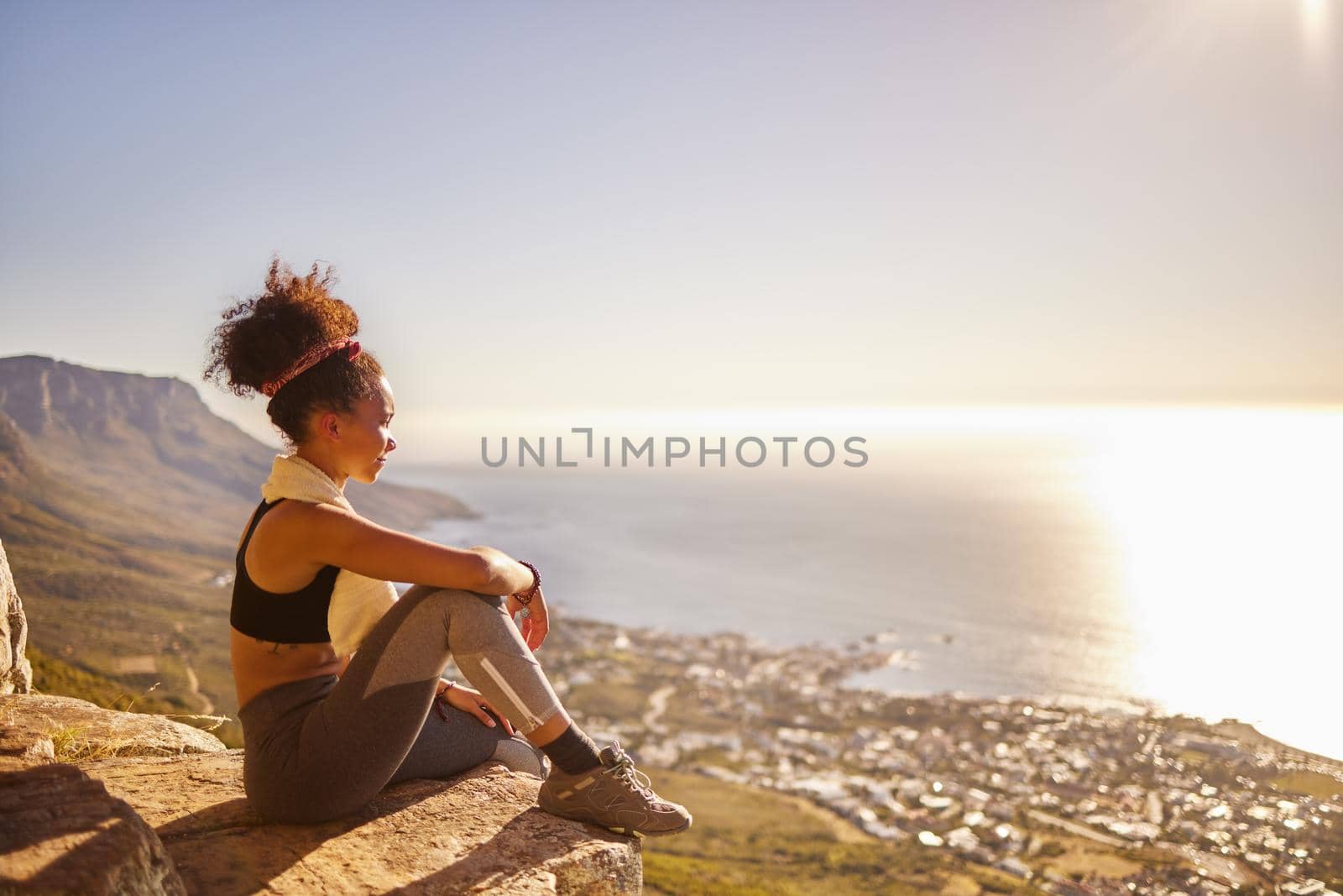 Working out indoors is just not as rewarding. a young woman looking at the view while sitting on a mountain cliff. by YuriArcurs