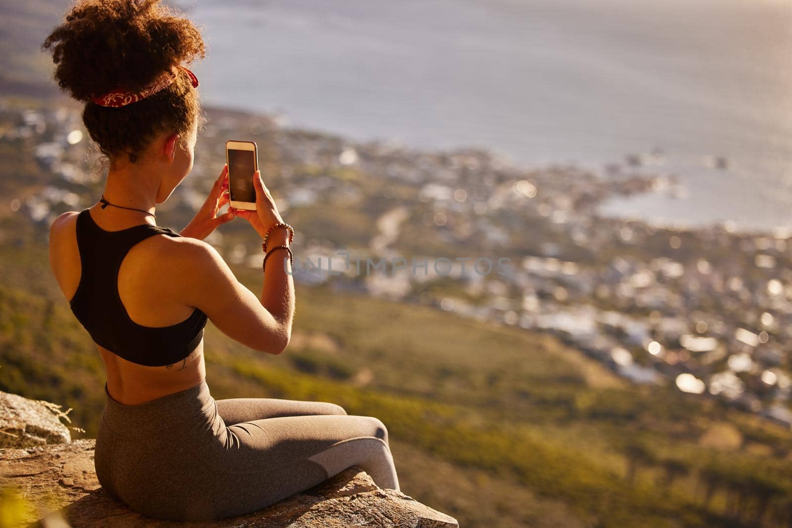 I want people to see how beautiful it is out here. a woman taking pictures with her cellphone while sitting on a mountain cliff