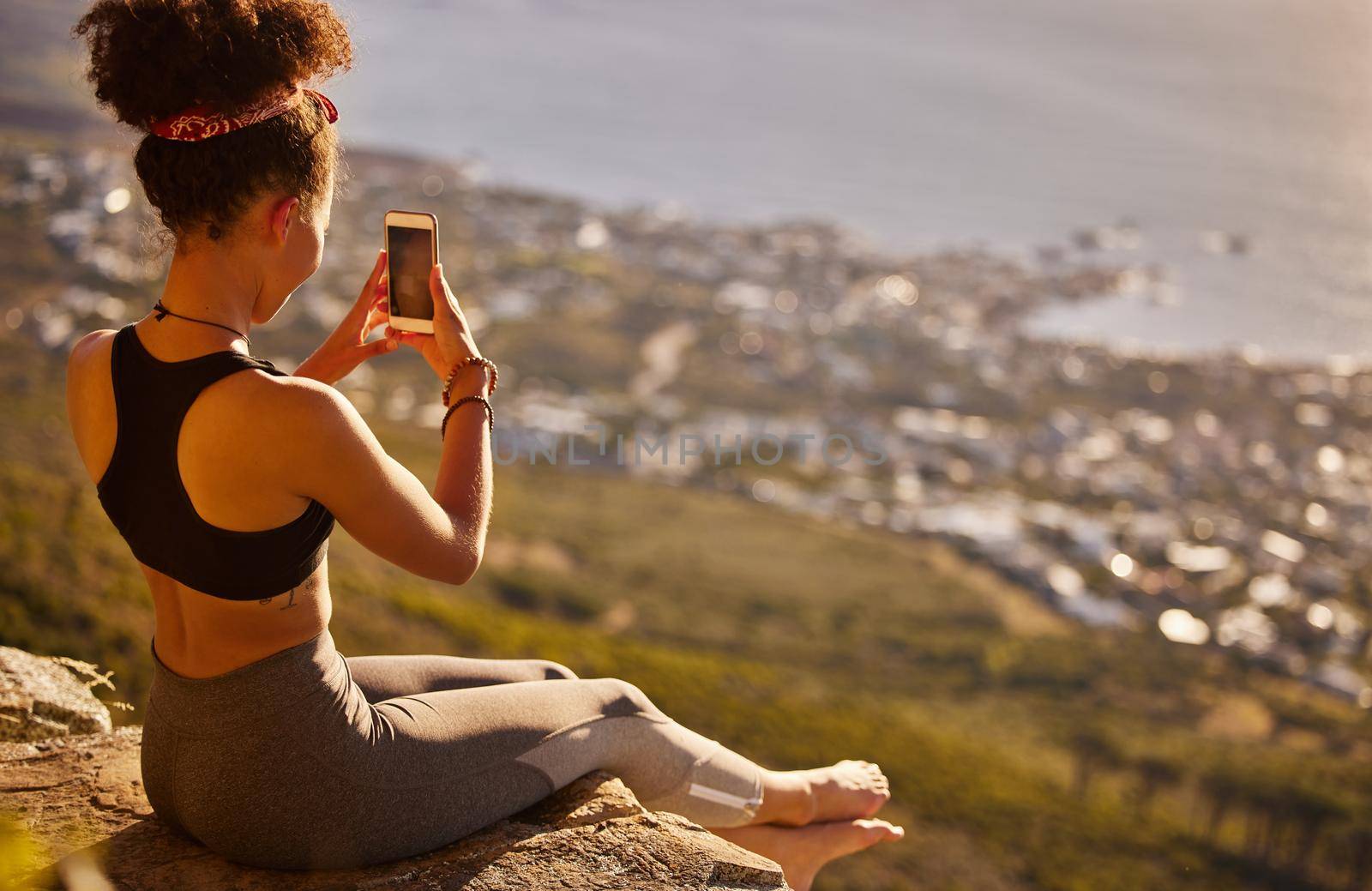I enjoyed the climb but the view is even more worth it. a woman taking pictures with her cellphone while sitting on a mountain cliff. by YuriArcurs