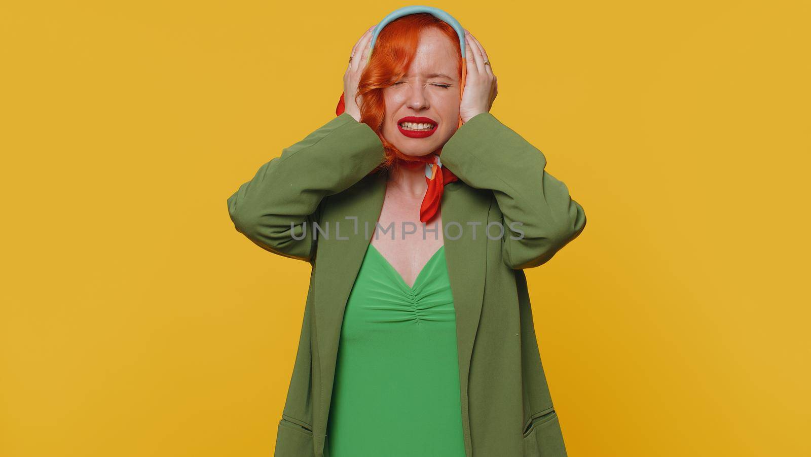 Redhead young woman in jacket rubbing temples to cure headache problem, suffering from tension and migaine, stress, grimacing in pain, high blood pressure. Girl isolated alone on yellow background