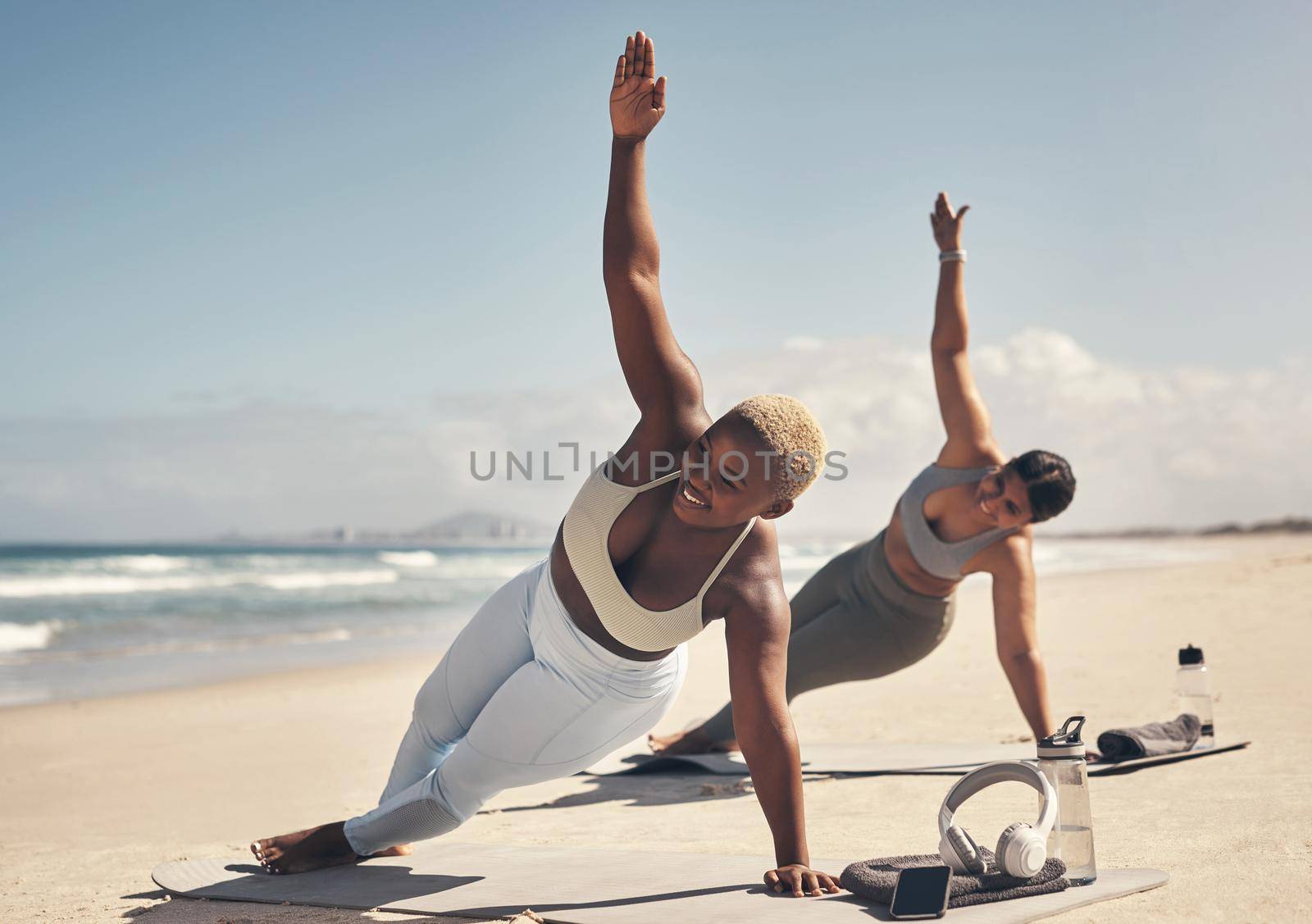 You can do yoga anywhere, anytime. two young women practicing yoga on the beach. by YuriArcurs