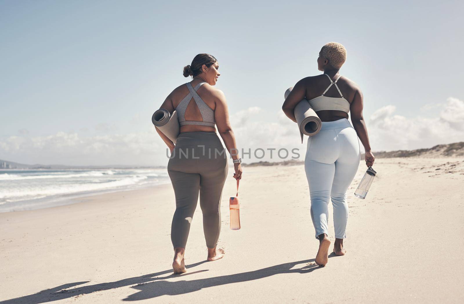 Weve made it a priority to practice yoga regularly. two young women walking on the beach with their yoga mats