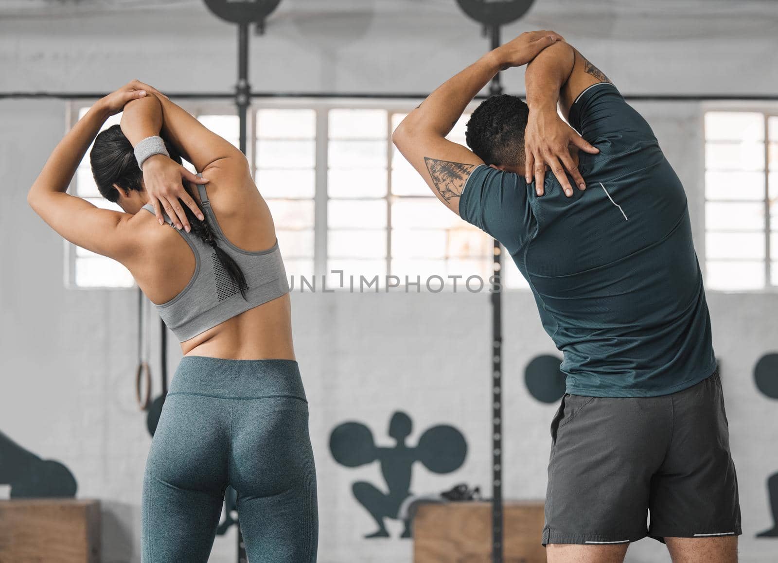 Active, sporty fitness couple stretching or gym partners and friends getting ready to exercise together. Back view of male trainer and female athlete standing and doing warm ups before workout class. by YuriArcurs