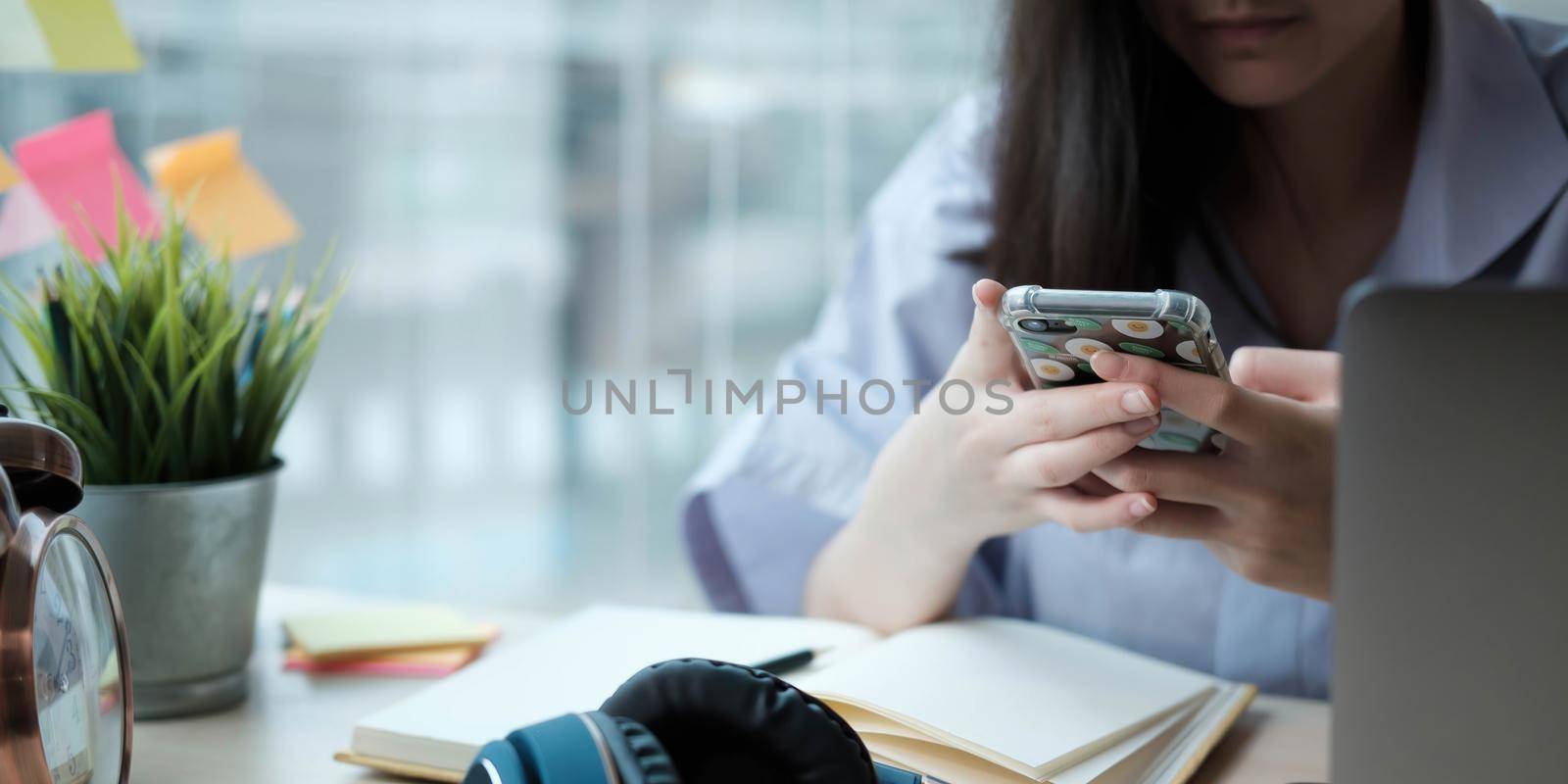 Female student taking notes from a book and using smart phone at home by wichayada