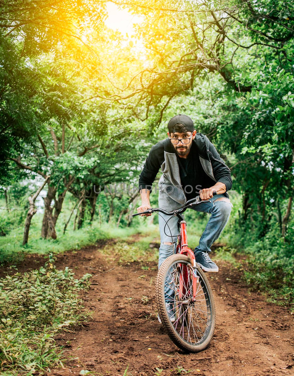 A guy riding a bike in the countryside, Person riding a bike in the countryside, Portrait of a guy in cap riding a bike on a country road, Bicyclist person on his bike on a country road forest.