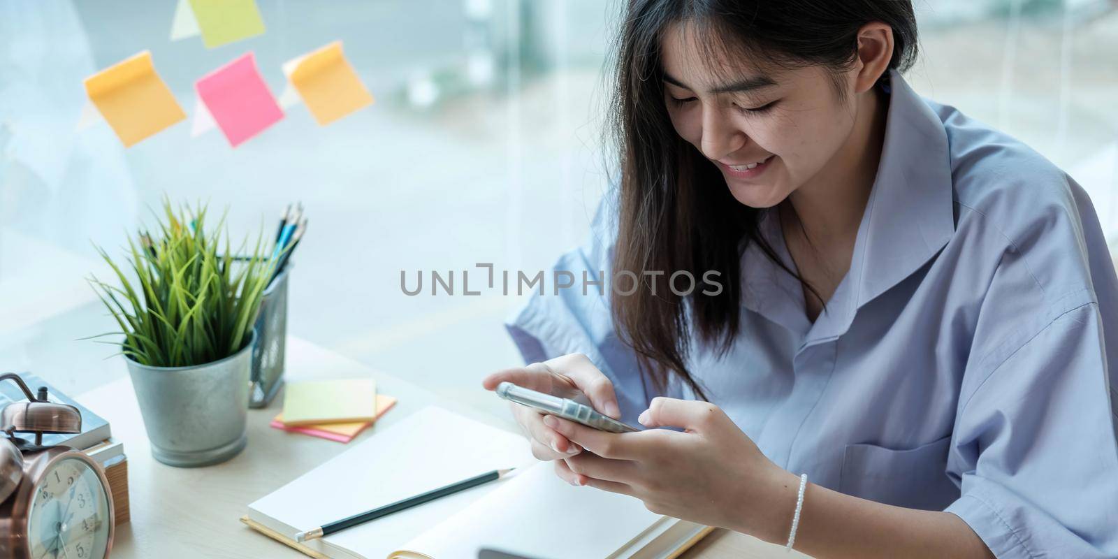 Female student taking notes from a book and using smart phone at home.