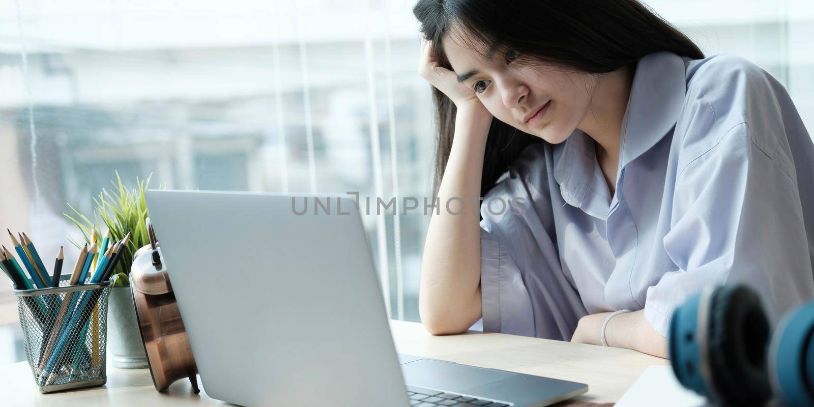 Asian girls are sitting stressed studying online with a tutor on a laptop while sitting in the bedroom at home night. Concept online learning at home by wichayada