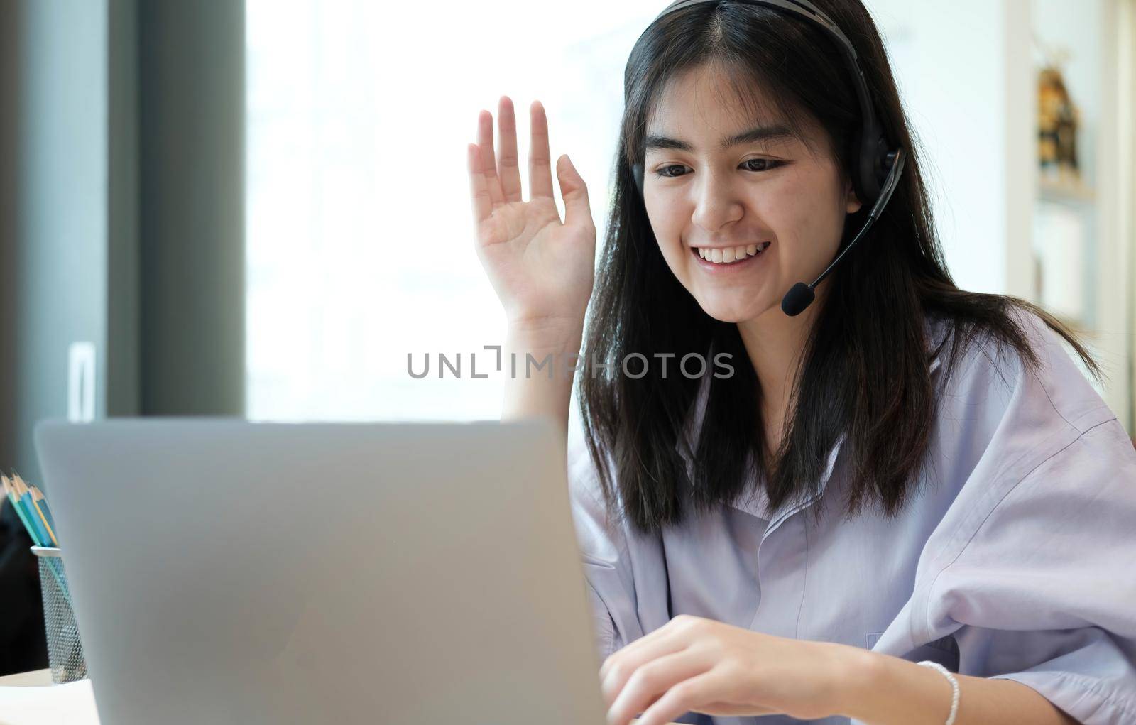 Smiling Asian young female using headset looking at laptop screen listen and learning online courses. Happy chinese business woman with headphones video call for customer service.