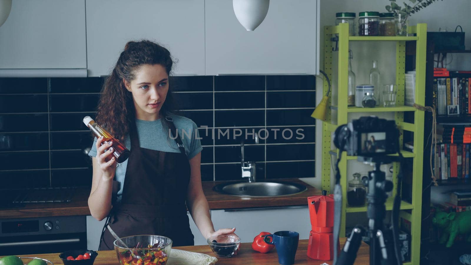 Cheerful attractive woman recording video food vlog about healthy cooking on digital camera in the kitchen at home. Vlogging and social media concept by silverkblack