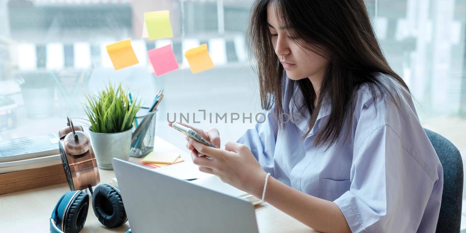 Female student taking notes from a book and using smart phone at home by wichayada