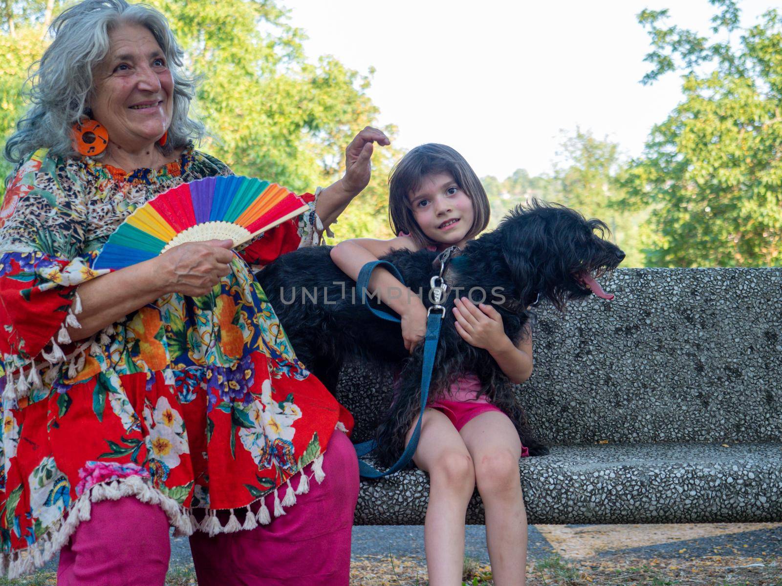 grandma , granddaughter and dog enjoying outdoors on a bench by verbano