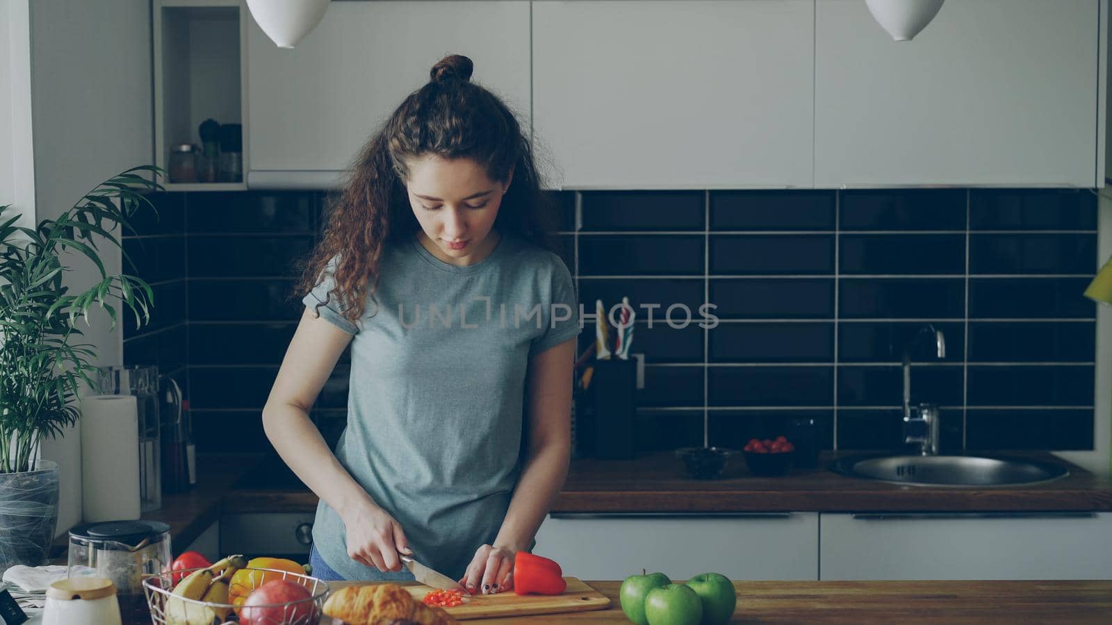 Curly beautiful caucasian woman in headphones dancing prepearing breakfast in kitchen at home