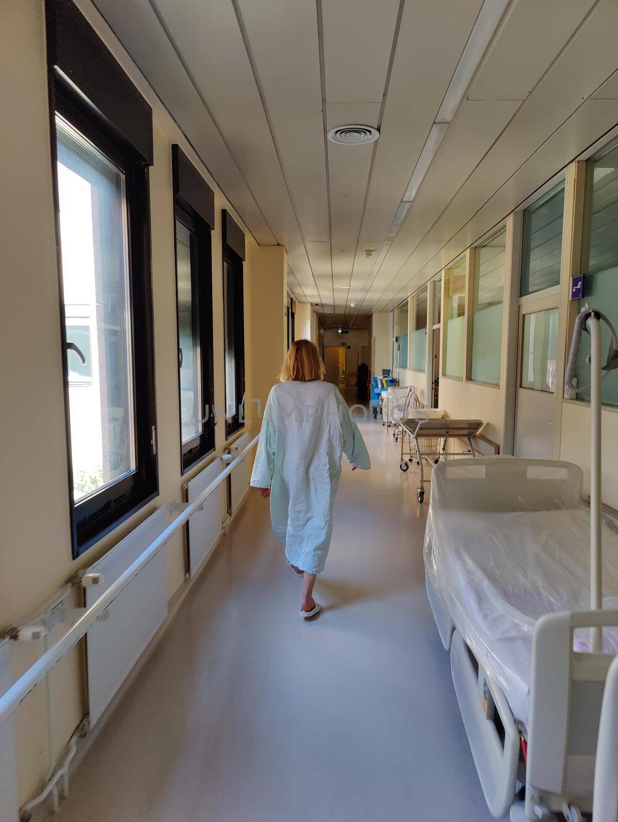Female patient wearing hospital robe walking in long empty hospital hallway