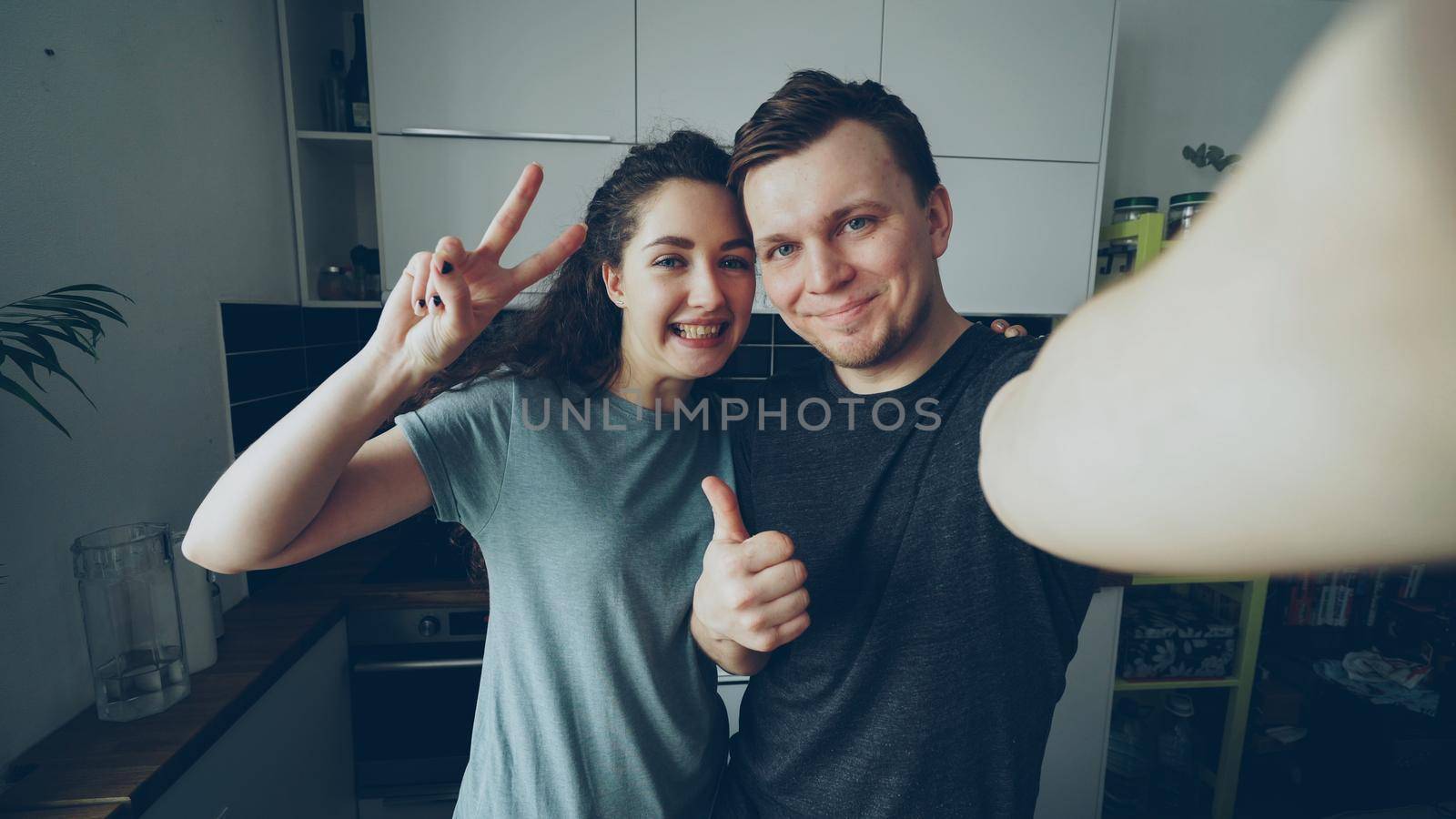 POV of Young funny couple taking selfie photos holding smartphone camera standing in the kitchen at home in the morning