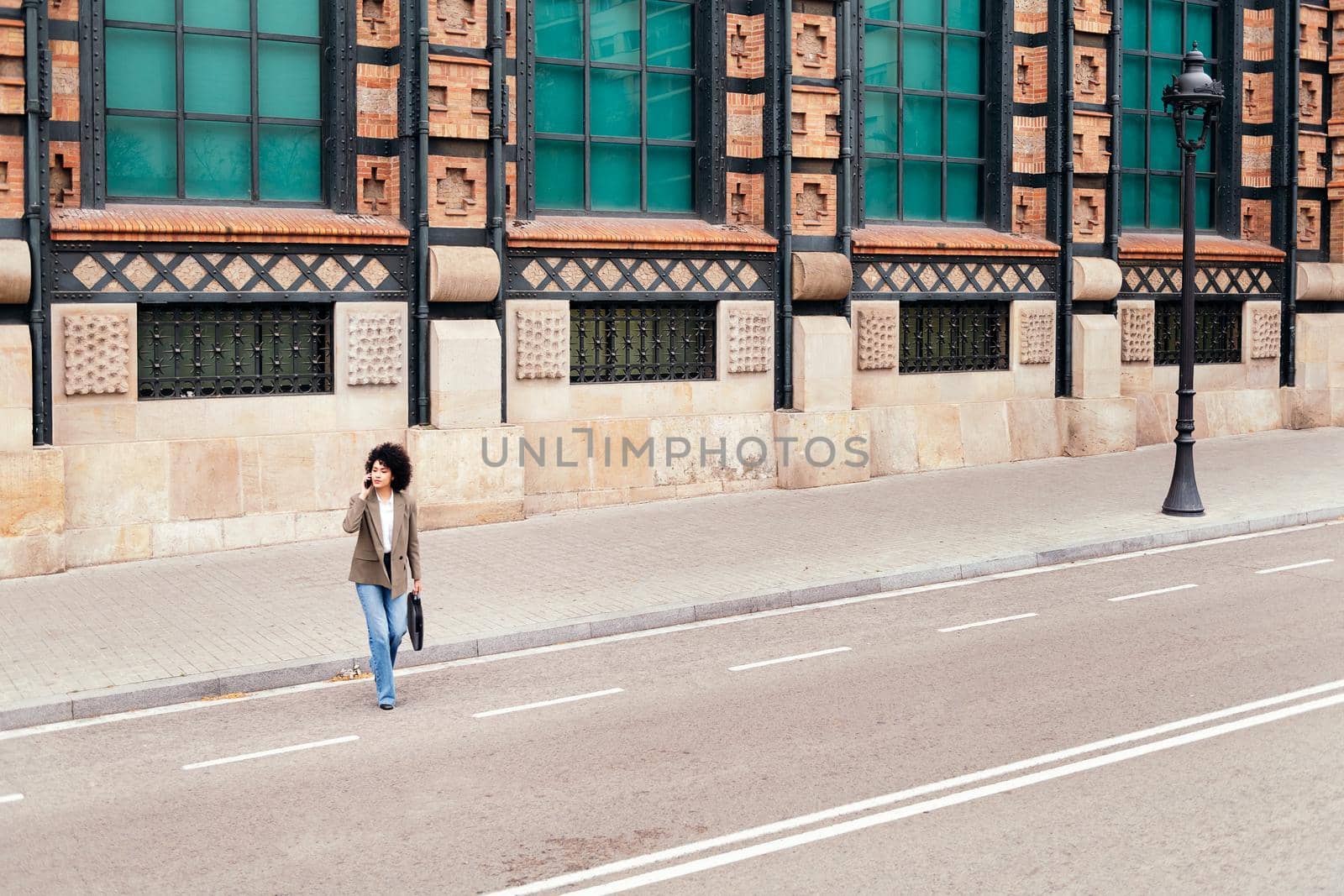 successful business woman walking across the street talking by phone with a briefcase in her hand, concept of urban lifestyle and technology, copy space for text