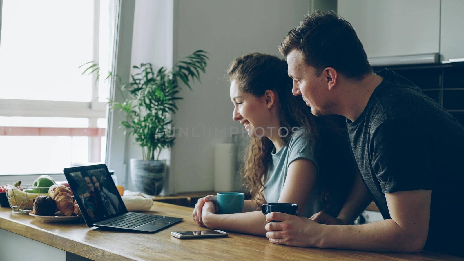 young beautiful caucasian couple sitting in modern kitchen at table in front of laptop talking with two girls, they are smiling and laughing