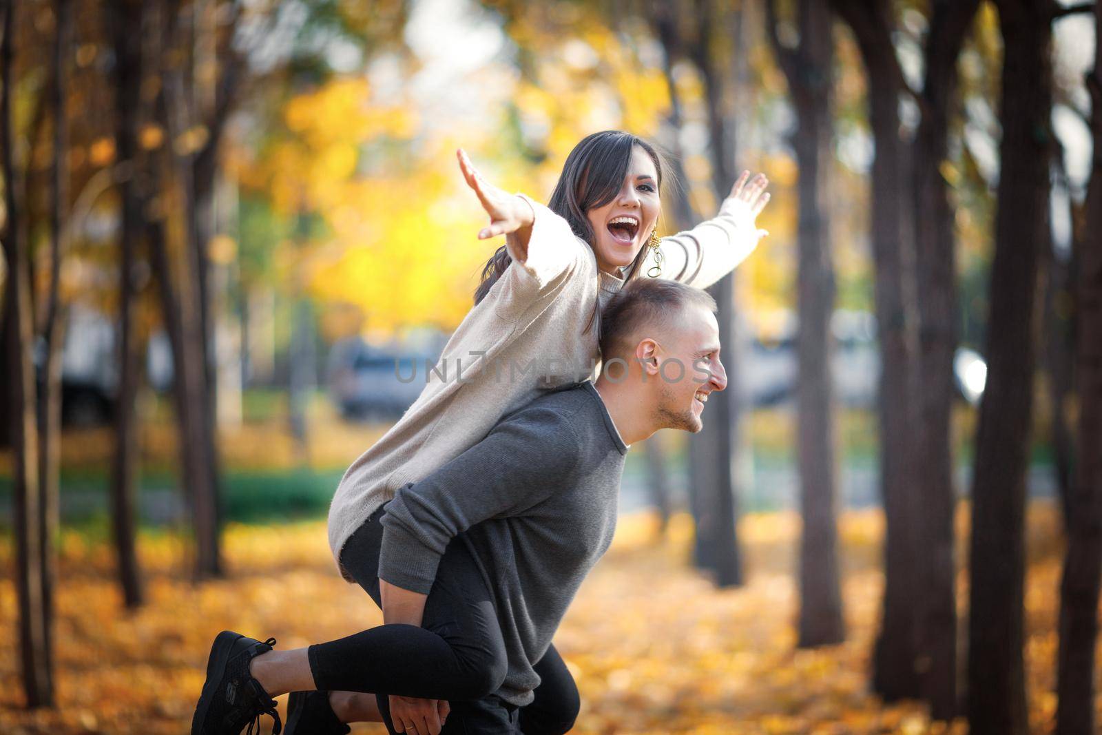 Happy smiling man carrying his laughing girlfriend on back in autumn nature.