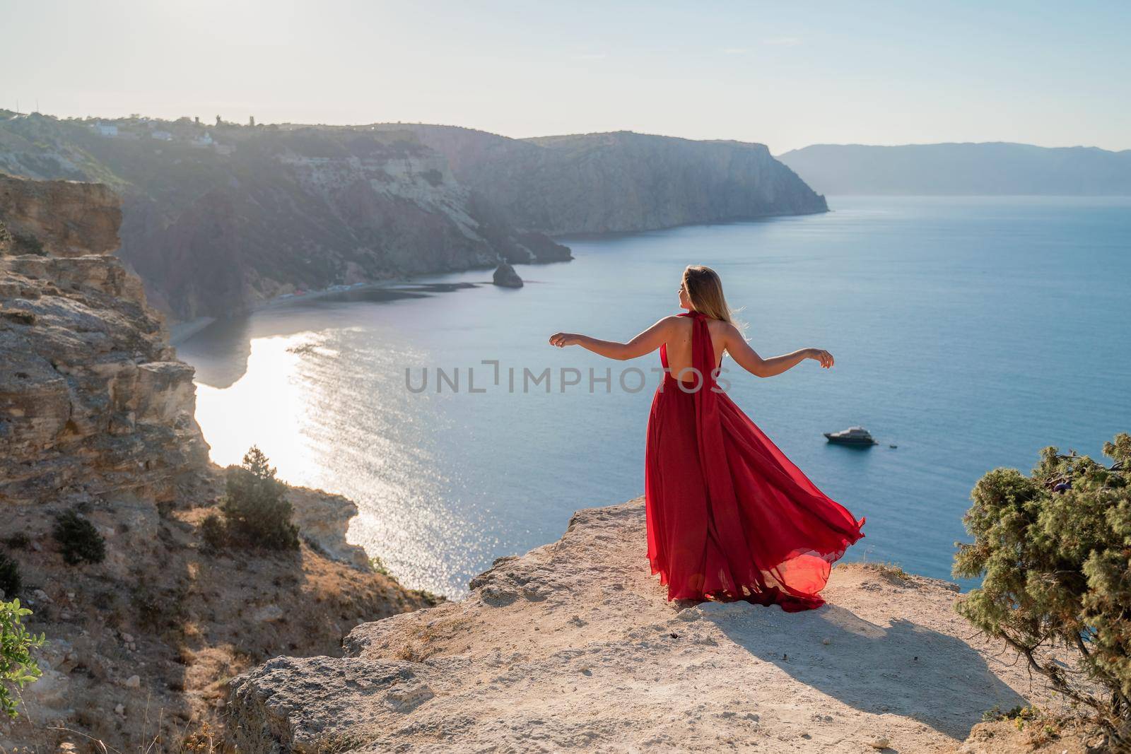 A woman in a red flying dress fluttering in the wind, against the backdrop of the sea