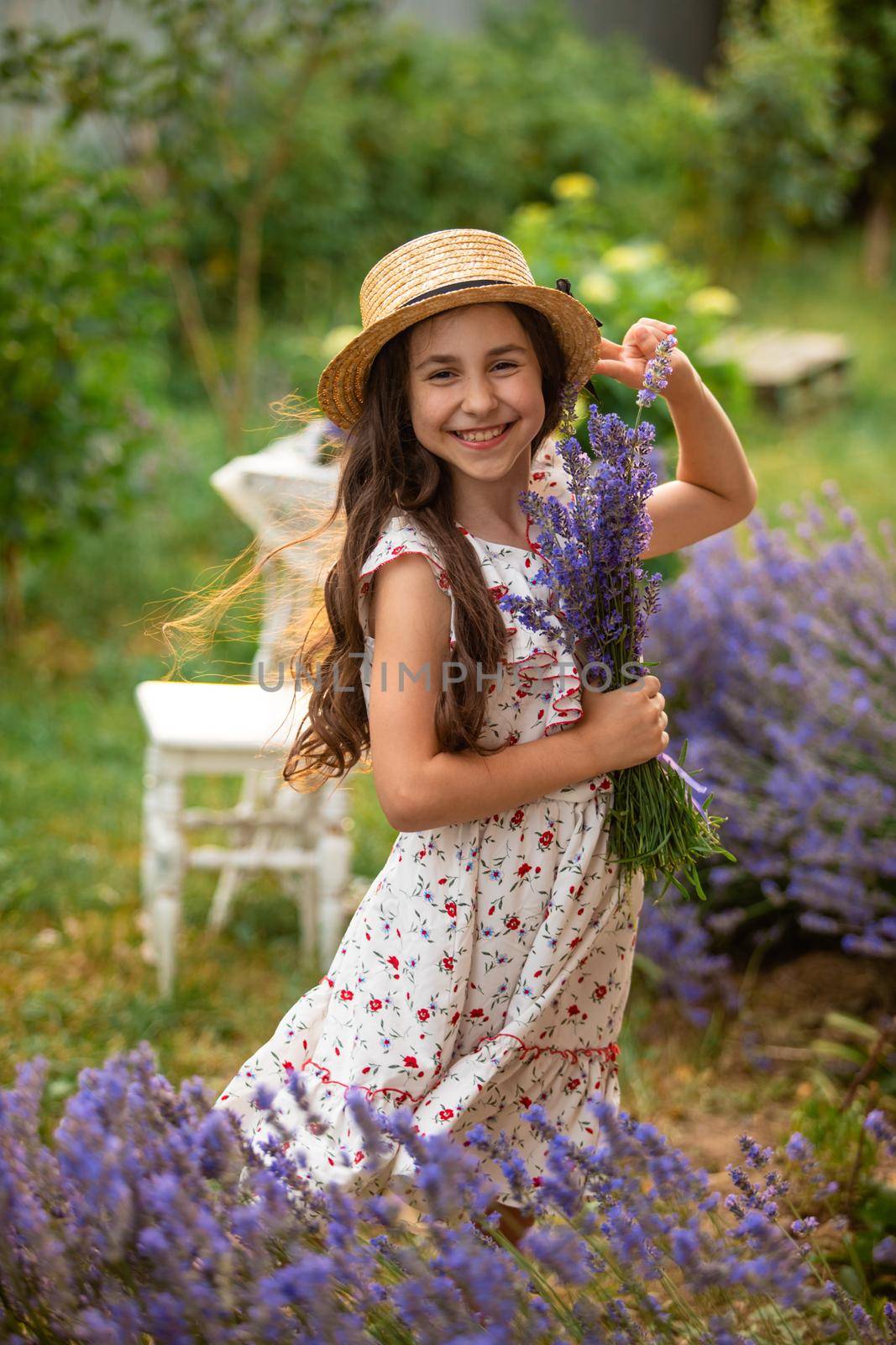 Beautiful long hair girl near lavender bushes at the garden. The girl is walking in the yard and collect flowers. A girl in a hat and dress.